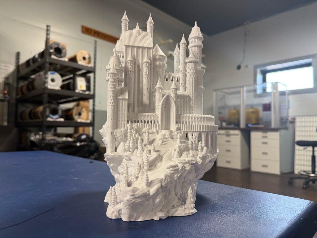 White 3D-printed castle model on a workshop table with filament spools behind it