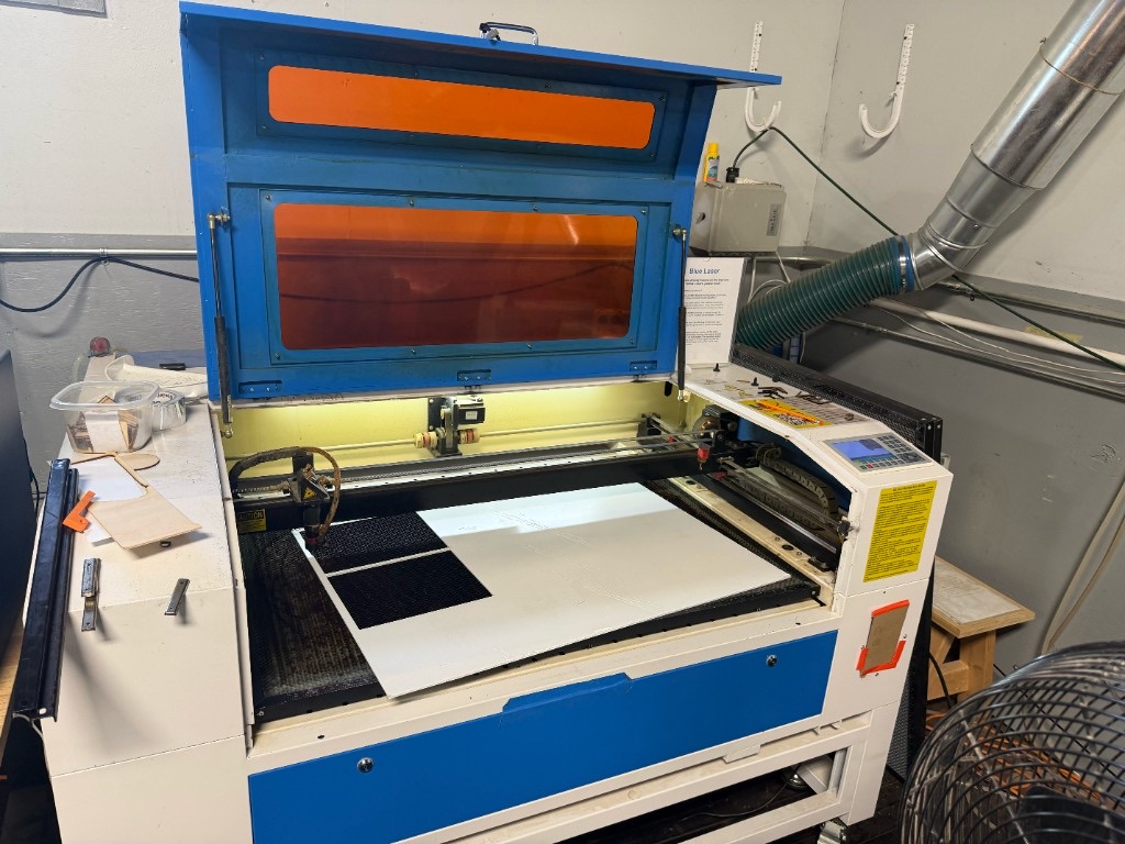 Open blue laser cutter with a sheet on the honeycomb bed and cut parts removed