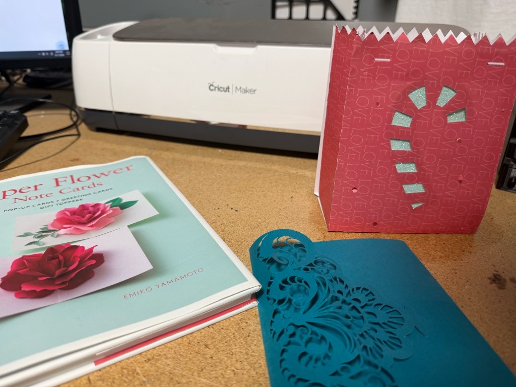 Paper crafts and a Cricut Maker on a desk with cut cardstock and a gift bag