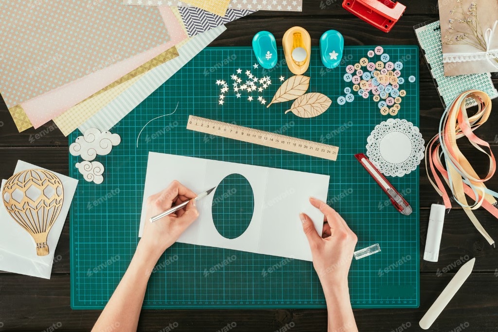 Hands using a craft knife to cut cardstock on a green cutting mat
