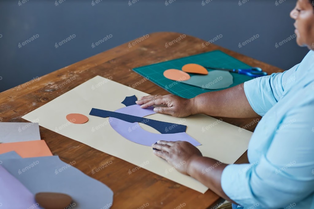 Maker arranging colored paper shapes into a collage on a wooden table