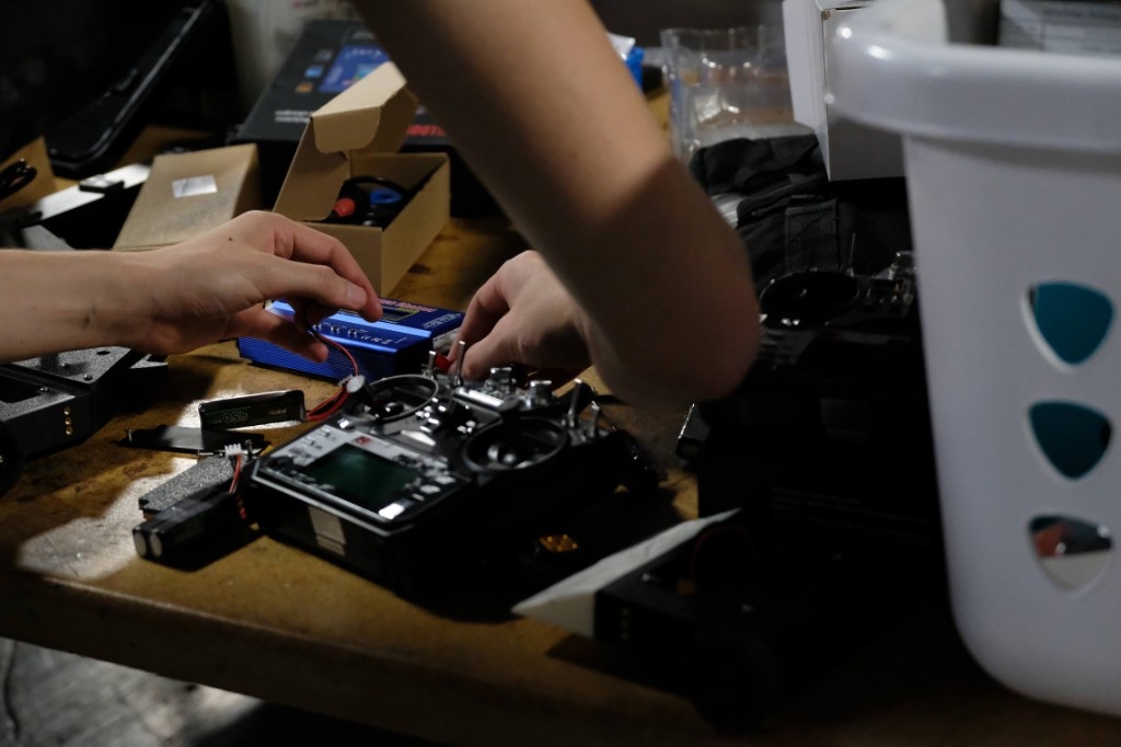 Hands working with a radio transmitter, battery charger, and LiPo batteries on a workbench